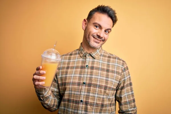 年轻英俊的男子喝着健康的橙汁 用稻草盖住黄色的背景 笑容满面 露出自信的笑容 露出牙齿 — 图库照片