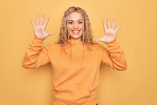 금발의 아름다운 여자가 스웨트 셔츠를 자신감 행복하게 웃으면서 손가락으로 번째를 — 스톡 사진