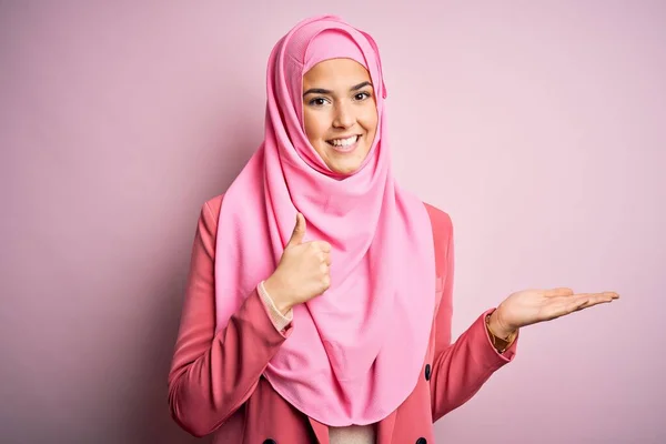 年轻美丽的女孩 戴着穆斯林头巾 站在孤立的粉色背景上 手牵着手 竖起大拇指 做着一个不错的手势 笑容满面 开朗愉快 — 图库照片