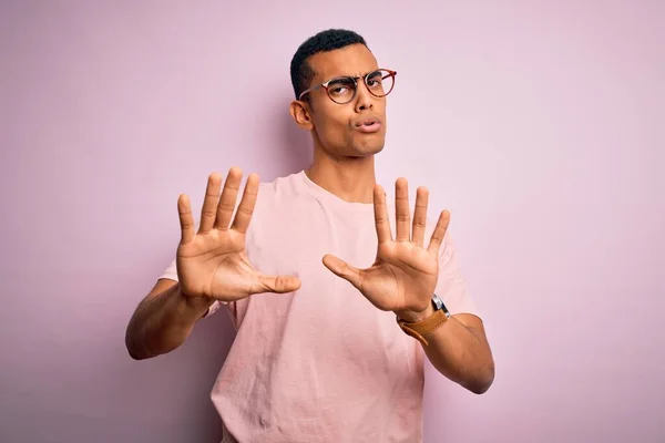 英俊的非洲裔美国男人 身穿休闲装 戴着粉色背景的眼镜 手心移开 带着恐惧和厌恶的表情 表示拒绝和否认 停止和禁止 — 图库照片