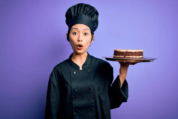 中国女厨师身穿炊事服 头戴礼帽 手里拿着蛋糕 吓着了一大跳 脸上带着惊讶的表情 害怕又兴奋 — 图库照片