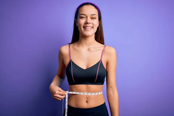 美しいですスリム女の子制御重量使用測定テープ上腰上紫色の背景に幸せな顔立ちと笑顔で自信を持って笑顔示す歯 — ストック写真