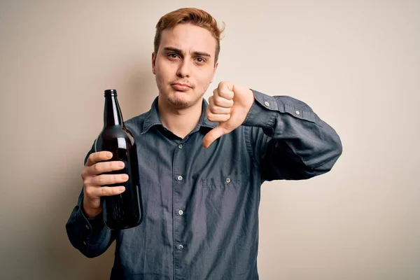 若いハンサムな赤毛男は怒った顔でビールのボトルを飲みます 親指で嫌いを示す負の記号ダウン 拒絶概念 — ストック写真