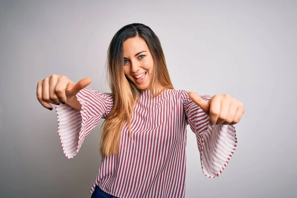 Young beautiful blonde woman with blue eyes wearing stiped t-shirt over white background approving doing positive gesture with hand, thumbs up smiling and happy for success. Winner gesture.