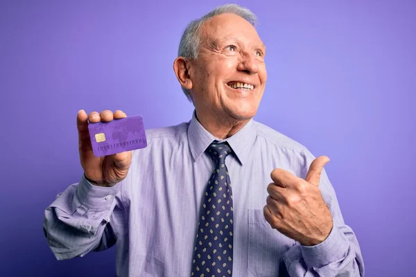 Senior Gråhårig Affärsman Håller Kreditkort Över Lila Bakgrund Pekar Och — Stockfoto