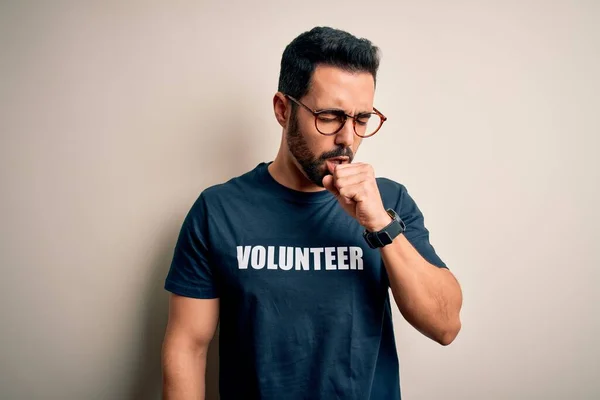 Handsome man with beard wearing t-shirt with volunteer message over white background feeling unwell and coughing as symptom for cold or bronchitis. Health care concept.