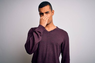 Beyaz arka plan üzerine gündelik kazak giyen genç, yakışıklı Afro-Amerikan erkeği pis ve iğrenç bir koku alıyor, nefes nefese kalmış, parmakları burnunda. Kötü kokuyor.