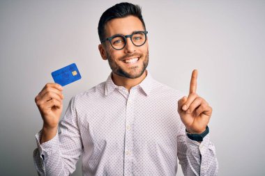 Genç bir iş adamı kredi kartını soyutlanmış arka planda tutarken bir fikre ya da soru işaretine şaşırır ve mutlu yüzle işaret eder.