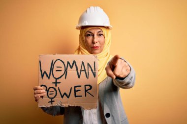 Orta yaşlı mimar kadın, elinde bayrak, elinde bayrak, elinde kadın mesajı, kamerayı işaret ediyor. Ve sen, el işareti, ön taraftan olumlu ve kendinden emin bir hareket.