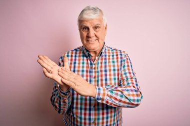 Kıdemli yakışıklı, beyaz gömlekli, pembe arka plan alkışı ve mutlu ve neşeli, gülümseyen, gururlu elleri birlikte alkışlayan bir adam.
