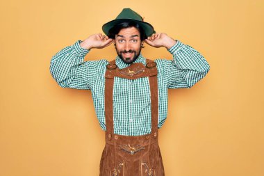 Almanya festivali için geleneksel Alman Ekim Festivali kıyafeti giyen yakışıklı genç adam parmaklarıyla kulaklarını çekerek gülüyor, komik bir jest. Seçme sorunu