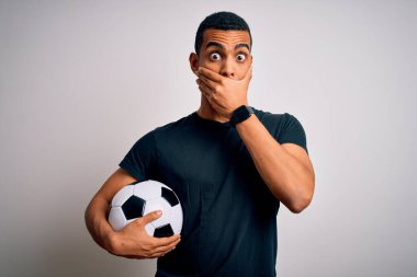 Beyaz arka planda futbol topu tutan yakışıklı Afro-Amerikalı adam yanlışlıkla ağzını kapatarak şok geçirdi. Gizli konsept.
