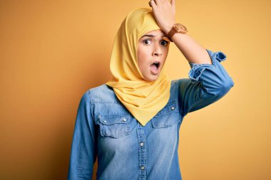 İslami tesettür takan genç ve güzel bir kız izole edilmiş sarı arka planda duruyor. Hatayla el ele tutuşup şaşırmış. Hatayı hatırla. Unuttum, kötü hafıza konsepti.