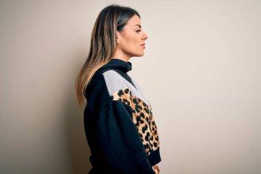 İzole edilmiş beyaz arka plan üzerinde duran, rahat profil pozu veren, doğal yüzlü ve kendinden emin gülümseyen genç, güzel bir kadın..