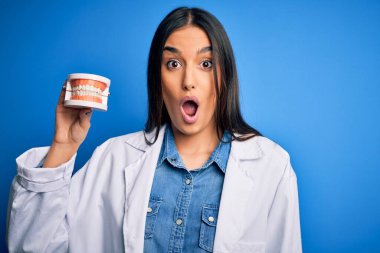 Plastik diş protezi tutan güzel, esmer dişçi kadın. Şaşırmış bir yüzle korkmuş, korku ifadesinden korkmuş ve heyecanlanmış.
