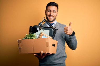 Ofis kasası tutan genç iş adamı sarı arka plandan kovuluyor. Kocaman gülümsüyor ve gülümsüyor. İşaret veriyor.