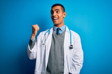 Mavi arka plan üzerinde steteskop ve ceket giyen yakışıklı Afro-Amerikan doktor gülümsüyor ve başparmağıyla yan tarafa bakıyor..