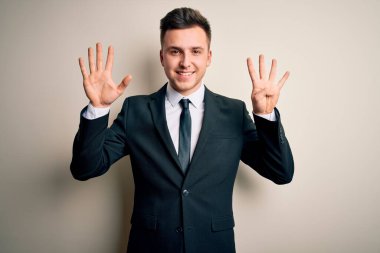 Zarif takım elbiseli ve kravatlı genç yakışıklı iş adamı izole edilmiş arka plan üzerinde dokuz numaralı parmaklarıyla işaret ederken kendinden emin ve mutlu gülümsüyor..