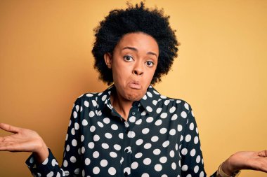 Kıvırcık saçlı, genç, Afro-Amerikan bir kadın. Hiçbir şeyden habersiz, elleri ve kolları havada, kafası karışmış bir şekilde dikiliyor. Şüphe kavramı.