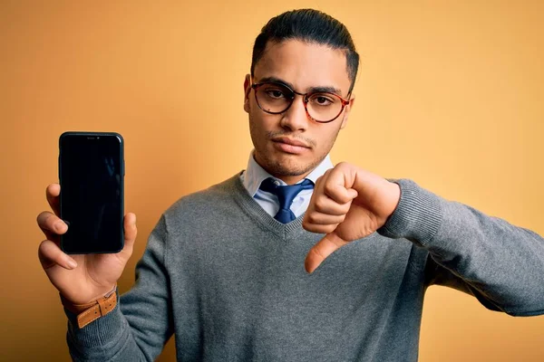 年轻的巴西商人戴着眼镜 手持智能手机 脸上带着愤怒的表情 脸上挂着不喜欢戴大拇指的负面标志 拒绝的概念 — 图库照片