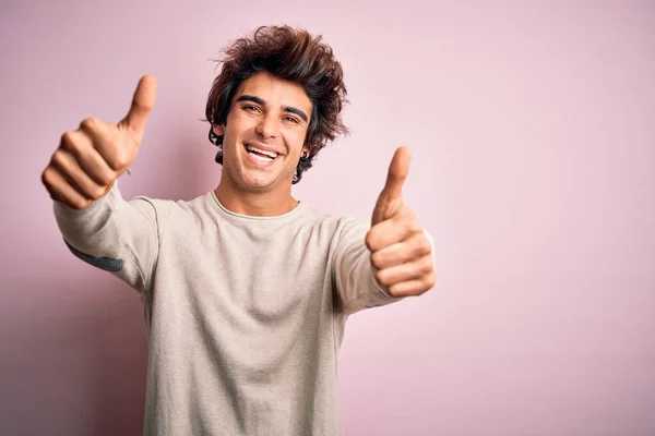 孤立したピンクの背景の上に立つカジュアルなTシャツを着た若いハンサムな男は 手で積極的なジェスチャーを行うことを承認し 親指を上げて笑顔と成功のために幸せ 勝者のジェスチャー — ストック写真