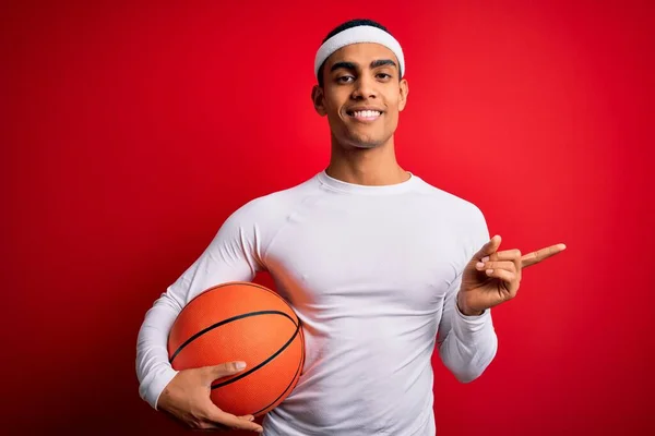 Joven Atleta Afroamericano Guapo Sosteniendo Pelota Baloncesto Sobre Fondo Rojo — Foto de Stock