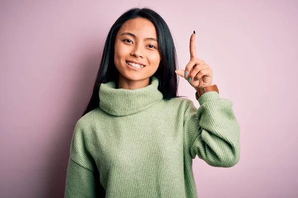 年轻美丽的中国女人穿着高领毛衣 披着孤立的粉色背景 用手指指尖着成功的点子 又兴奋又快乐第一部分 — 图库照片