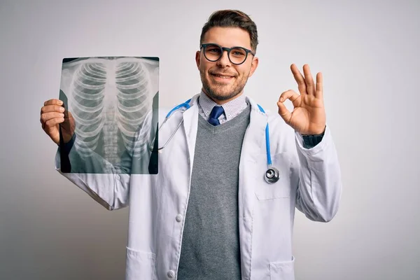 年轻的医生穿着医疗外套 用手指在孤立的背景下检查胸部X线片 做了个好手势 很好的符号 — 图库照片