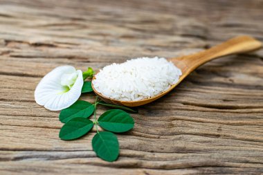 Tahta bir kaşıkta yasemin pilavı ve tahta bir masada beyaz anchan çiçekleri.