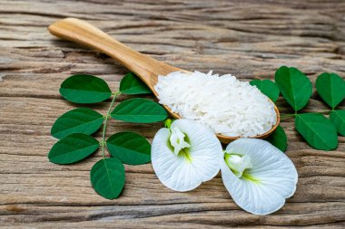 Tahta bir kaşıkta yasemin pilavı ve tahta bir masada beyaz anchan çiçekleri.