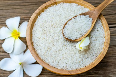 Tahta bir kasede yasemin pilavı, tahta kaşıklar ve eski ahşap bir masanın üzerinde tesisat çiçekleri.