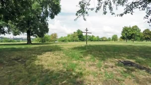 Křesťanský kříž stojí na zelené pole u lesa. — Stock video