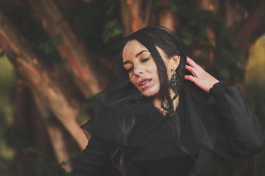 Siyah elbiseli ve peçeli kadın bir ağacın yanında