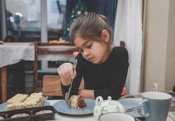 girl sits at a table and picks a cake