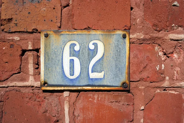 House Number 62 sign. Weathered enamelled blue Number sixty-two plate mounted on a brick wall.