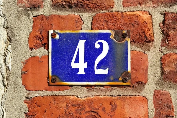 House Number 42 sign. Rusty enamelled house number forty-two plate mounted on a brick stone wall.