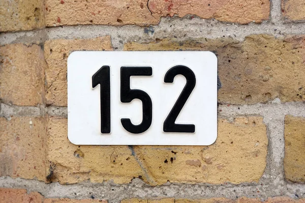 House Number 152 sign. White Number one hundred and twenty-five plate mounted on a brick wall.