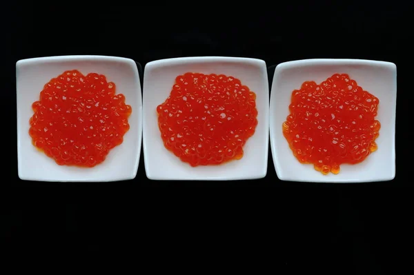 Caviar rojo en tazón blanco sobre fondo de vidrio negro —  Fotos de Stock