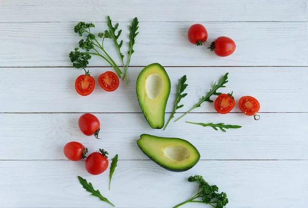 Nature morte avec avocat, tomates cerises, roquette et persil sur fond de bois blanc. pose plate — Photo