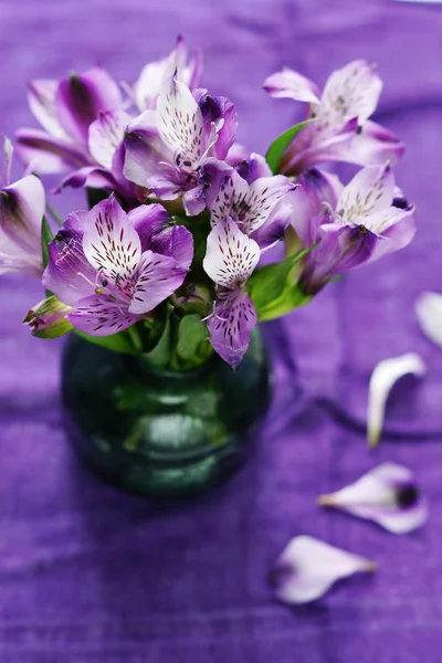 Букет свежих фиолетовых цветов в зеленой вазе на фиолетовом фоне льна — стоковое фото