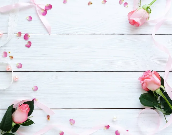 Marco de escritorio femenino con rosas rosadas y pétalos sobre fondo de madera blanco. Asiento plano, vista superior. Fondo de flores. Día de la mujer, día de la madre . — Foto de Stock