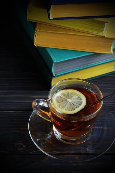 Szkło kubek z gorącą herbatę z cytryną na tle książek w kolorowe Pokrowce — Zdjęcie stockowe
