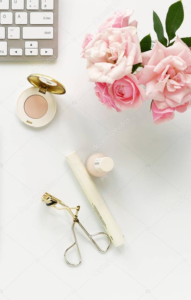 Beauty blog concept. Female make up accessories and bouquet of pink roses on white background. Flat lay, top view feminine desk, workspace with laptop. 