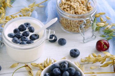 Bir lezzetli ve sağlıklı kahvaltı granüller, küçük bir cam kavanoza Beyaz ahşap zemin üzerinde yaban mersini ile yoğurt.
