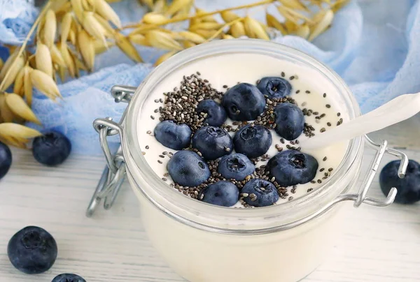 En god och hälsosam frukost färsk yoghurt med blåbär och chiafrön i en liten glasburk på en vit trä bakgrund. Närbild — Stockfoto