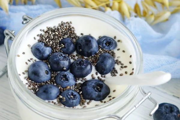 Ein leckeres und gesundes Frühstück mit frischem Joghurt mit Blaubeeren und Chiasamen in einem kleinen Glas auf weißem Holzhintergrund. — Stockfoto