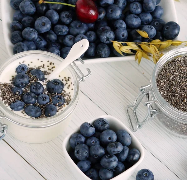En god och hälsosam frukost färsk yoghurt med blåbär och chiafrön i en liten glasburk på en vit trä bakgrund. Närbild — Stockfoto