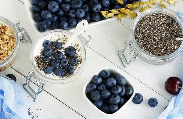 En god och hälsosam frukost färsk yoghurt med blåbär och chiafrön i en liten glasburk på en vit trä bakgrund. Närbild — Stockfoto