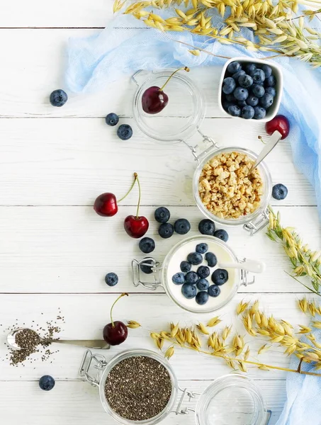 新鮮なブルーベリー顆粒、チアシード、白い木製の背景にガラスの瓶にブルーベリーとヨーグルトのおいしい健康的な朝食。トップ ビュー — ストック写真