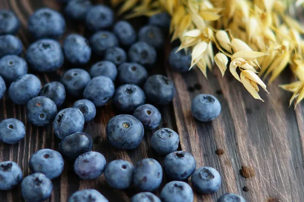 Bayas frescas de arándanos con espiguillas de avena maduras sobre fondo de madera oscura . — Foto de Stock